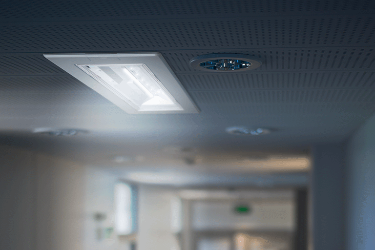 Ceiling close-up with recessed LED lights illuminating a dim hallway. Modern design evokes a neutral, sterile ambiance.